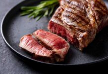 A beautifully grilled steak with a slice cut off, garnished with herbs
