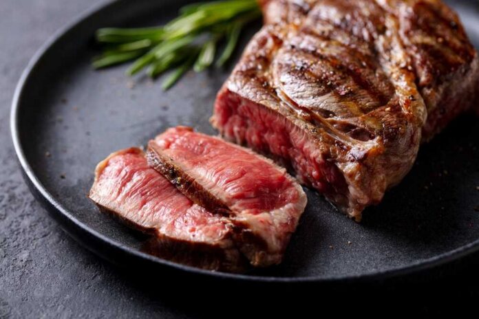 A beautifully grilled steak with a slice cut off, garnished with herbs
