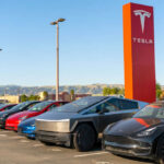 Tesla cars parked outside dealership with sign nearby
