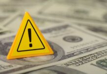 A yellow warning sign placed on a pile of dollar bills
