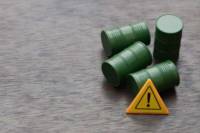 Warning,Symbol,Highlights,Economic,Risk,From,Rising,Oil,Prices Four green barrels and a warning sign on a wooden surface