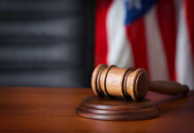 A wooden gavel resting on a sound block with an American flag in the background