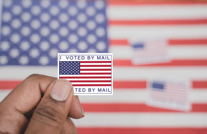 Hand holding a vote-by-mail sticker with U.S. flag