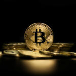 Gold Bitcoin coin on pile, dark background.