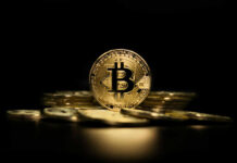 Gold Bitcoin coin on pile, dark background.