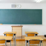 Empty classroom with desks, chalkboard, and clock.