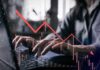 Person typing on a laptop with a declining stock market graph overlay