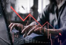 Person typing on a laptop with a declining stock market graph overlay