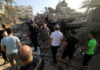 People examining rubble of collapsed building in sunlight.