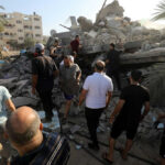 People examining rubble of collapsed building in sunlight.