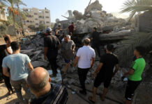 People examining rubble of collapsed building in sunlight.