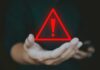 A hand holding a red warning triangle with an exclamation mark