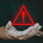 A hand holding a red warning triangle with an exclamation mark