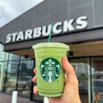 Hand holding a green matcha drink in front of a Starbucks store