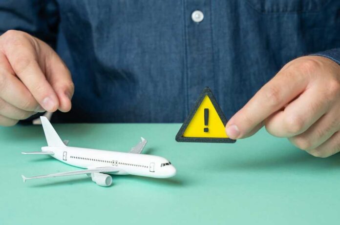 A,Man,Holds,A,Sign,Of,Attention,Near,A,Passenger A person holding a warning sign next to a model airplane