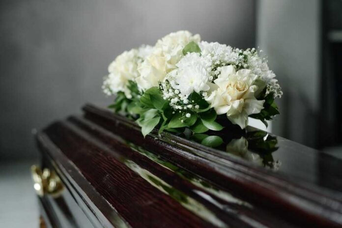A floral arrangement of white roses and greenery on a polished casket