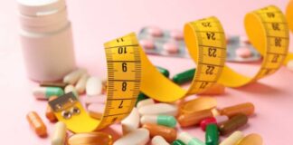 Assorted pills and a measuring tape on a pink background
