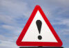 Warning road sign with exclamation mark against a cloudy sky