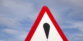 Warning road sign with exclamation mark against a cloudy sky