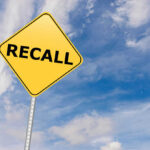 Yellow sign with RECALL text against blue sky.