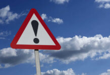 Warning sign with exclamation mark against sky