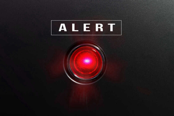 shutterstock_582441490-1 Red alert light against black background, text ALERT.