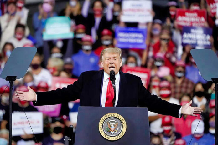 Donald Trump speaking at a rally with arms outstretched at a podium