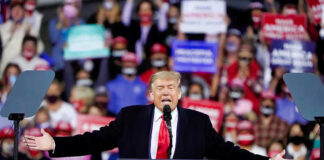 Donald Trump speaking at a rally with arms outstretched