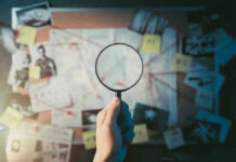 Magnifying glass over investigation board with photos and strings.