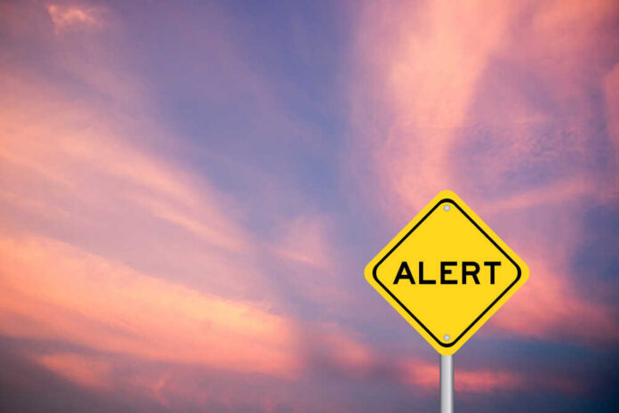 Yellow alert sign against a colorful sunset sky