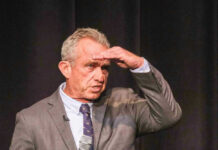 Robert F. Kennedy Jr. shielding his eyes while speaking on stage