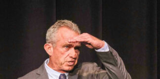 Robert F. Kennedy Jr. shielding his eyes while speaking on stage