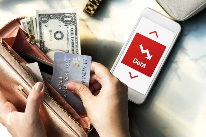 Person holding a credit card and cash while looking at a phone displaying debt information