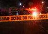 Crime scene tape with emergency vehicles in background.